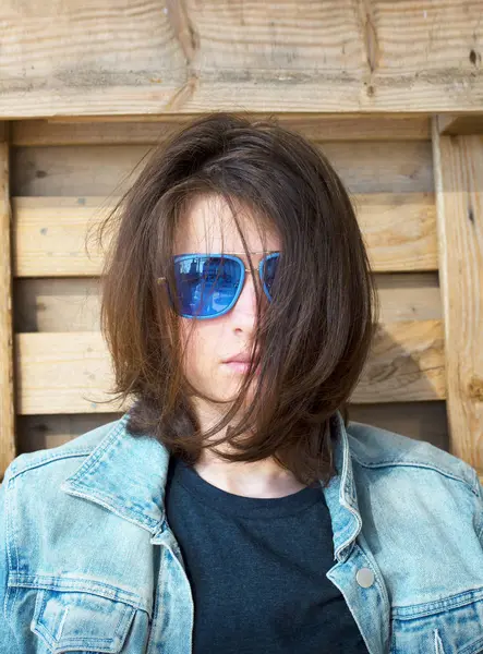 Young man in a jeans jacket and sunglasses sits on wooden pallets — Stock Photo, Image