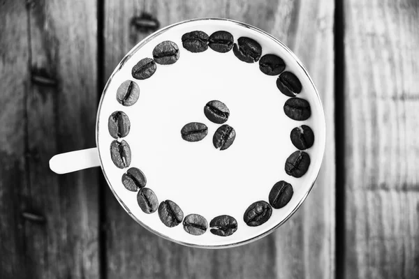 Kaffeebohnen in einer Tasse mit Milch auf einem Holztisch — Stockfoto