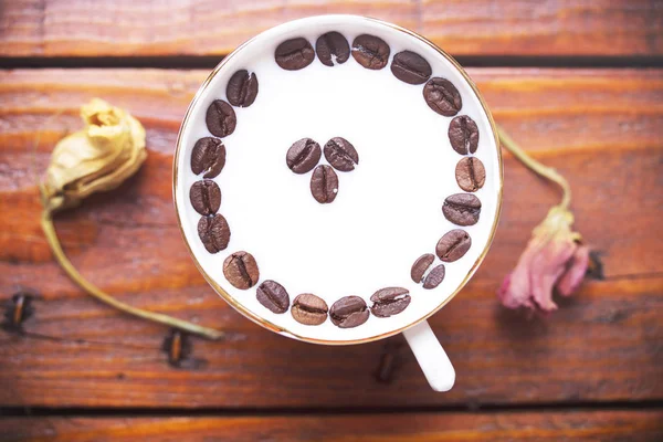 Kaffebönor i en kopp mjölk på ett träbord — Stockfoto