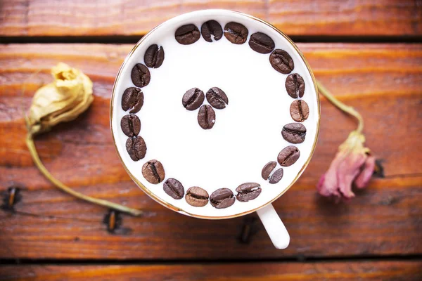 Kaffebönor i en kopp mjölk på ett träbord — Stockfoto