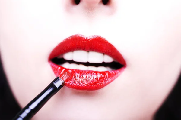 Foto de moda de maquillaje facial que demuestra los labios de una linda chica pintada con lápiz labial brillante con el hepl del cepillo . —  Fotos de Stock