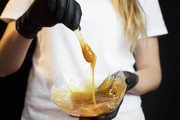 Woman with sugar hair removing paste on black background