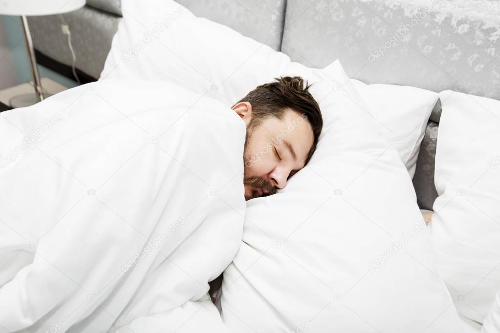 Attractive bearded young man sleeping in bed at home