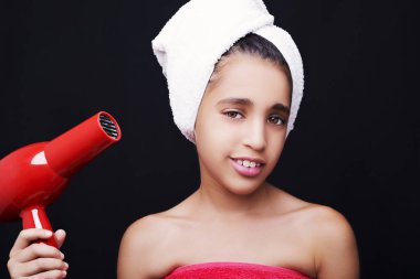  Kafasında havlu ve saç kurutma makinesiyle gülümseyen küçük bir kız.