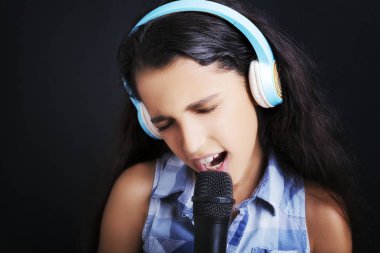 Mikrofon ve kulaklık kullanarak neşe ile şarkı söyleyen genç çekici kız 