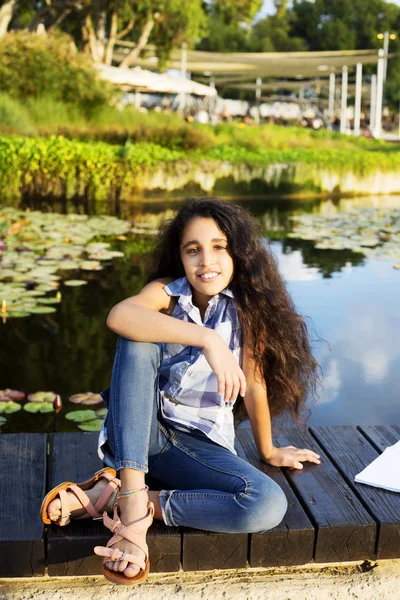 따뜻하고 화창한 여름 날에는 연못 근처에 앉아 귀여운 소녀 — 스톡 사진