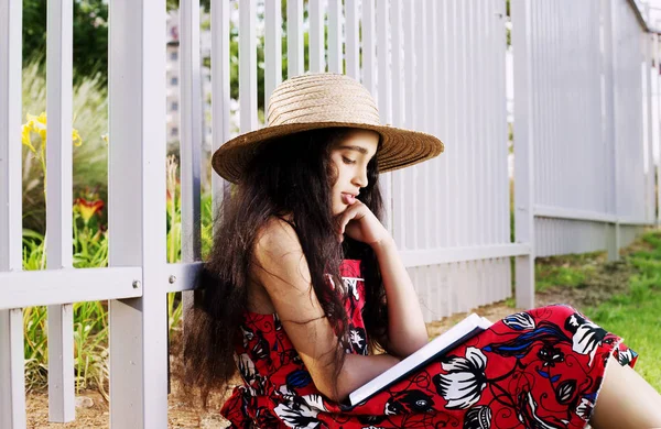 Adorável menina em vestido e chapéu livro de leitura no parque de verão . — Fotografia de Stock