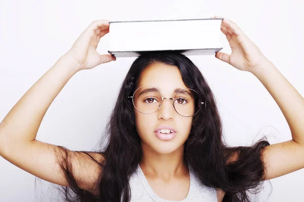 Menina adorável estudando com óculos e livro na cabeça — Fotografia de Stock