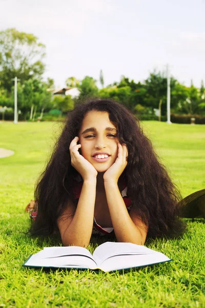 Das kleine afrikanische Mädchen liegt mit Buch auf einer Wiese im Park — Stockfoto