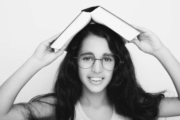 Adorable chica estudiando con gafas y libro en la cabeza — Foto de Stock