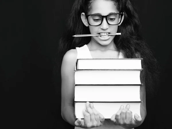 Petite fille avec des lunettes et un crayon tient des livres sur fond noir — Photo