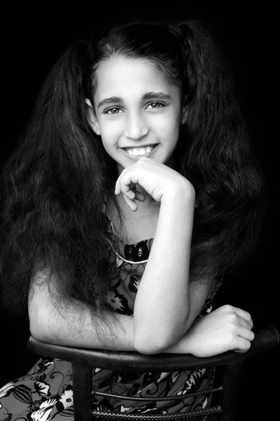 Gülümseyen ve kameraya bakarak bir sandalyede oturan güzel kız