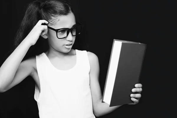 Adorable chica estudiando con gafas y libro en la mano —  Fotos de Stock