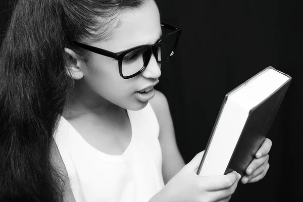Menina adorável estudando com óculos e livro na mão — Fotografia de Stock