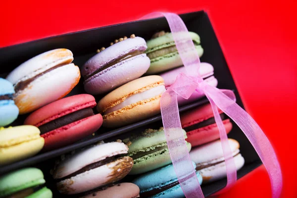 Tasty different colored macarons in black box on red background — Stock Photo, Image