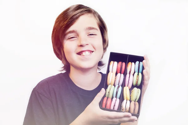 Счастливый улыбающийся мальчик держит десертные макароны в деревянной коробке — стоковое фото