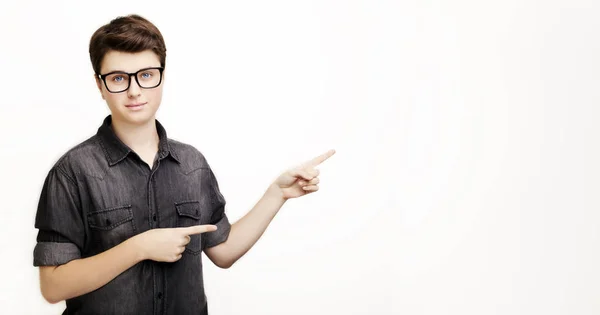 Feliz joven guapo hombre en gafas y jeans camisa apuntando lejos y sonriendo, mientras que de pie sobre fondo blanco —  Fotos de Stock