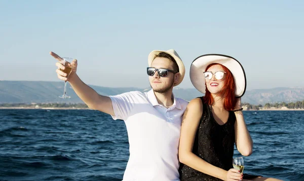 Hermosa pareja de amantes navegando en un barco. Dos modelos de moda posando en un velero al atardecer — Foto de Stock