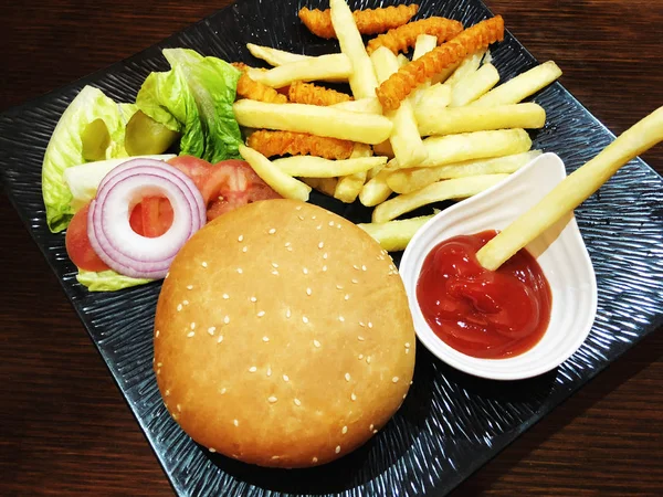 Hamburger na drewnianym stole na czarnej płycie. — Zdjęcie stockowe