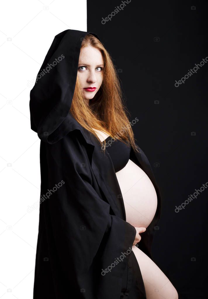 Beautiful redhead young pregnant woman in a black cloak with a hood.