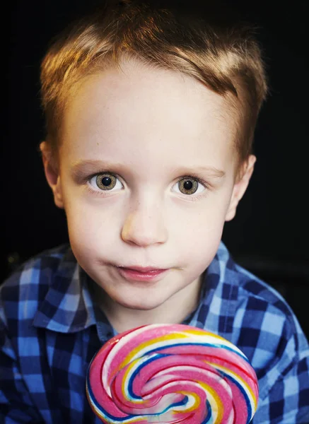 Young boy holding lollipop on black background. — Stock Photo, Image