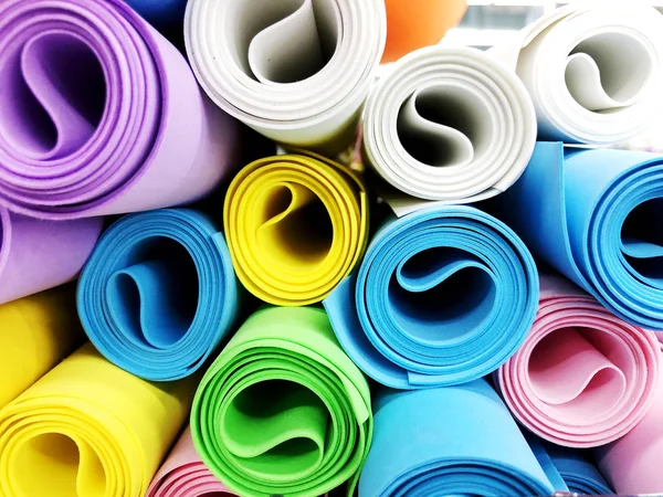 Many colorful yoga mats as background. Rolled yoga exercise mats against white