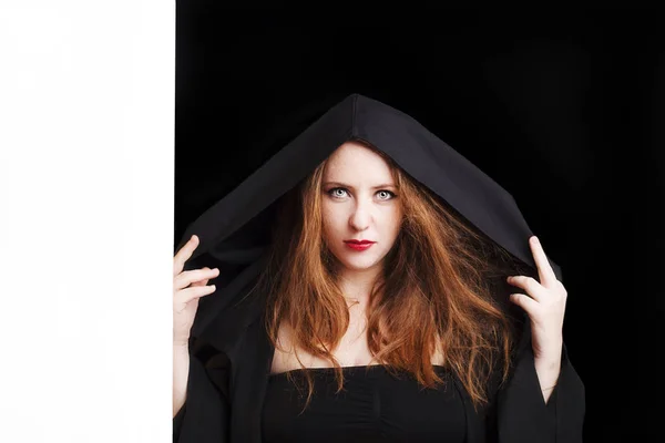 Beautiful redhead young pregnant woman in a black cloak with a hood. — Stock Photo, Image