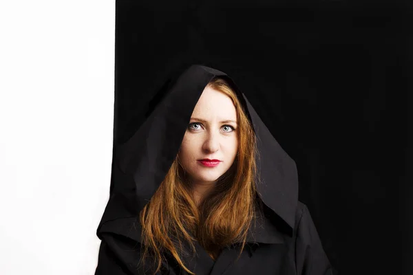 Schöne rothaarige junge Frau in einem schwarzen Mantel mit Kapuze. — Stockfoto