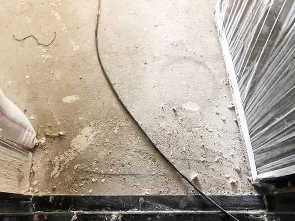 Sebuah kabel dan sekantong pasir di lantai kotor. Bahan untuk perbaikan di sebuah apartemen sedang dibangun, direnovasi, dibangun kembali, dan direnovasi . — Stok Foto