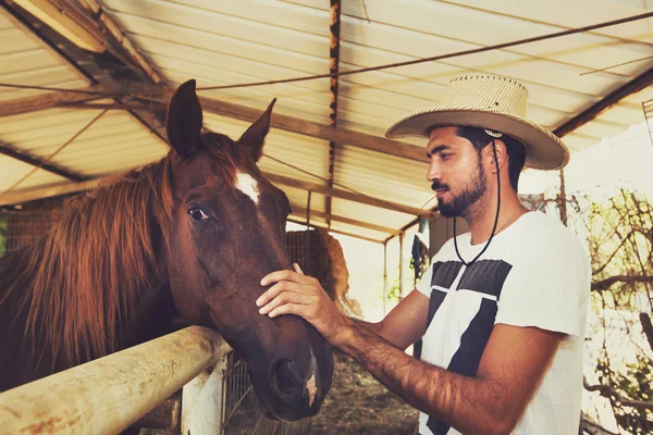 Jeune éleveur de chevaux réconfortant un cheval dans une écurie . — Photo