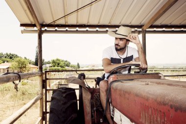 Genç çiftçi yaşlı bir traktörün direksiyonunda oturuyor.