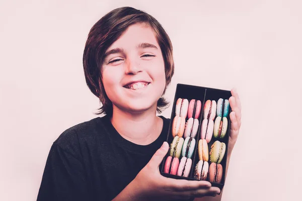 Gelukkig lachend jongen nagerecht macarons bedrijf in houten kist. — Stockfoto