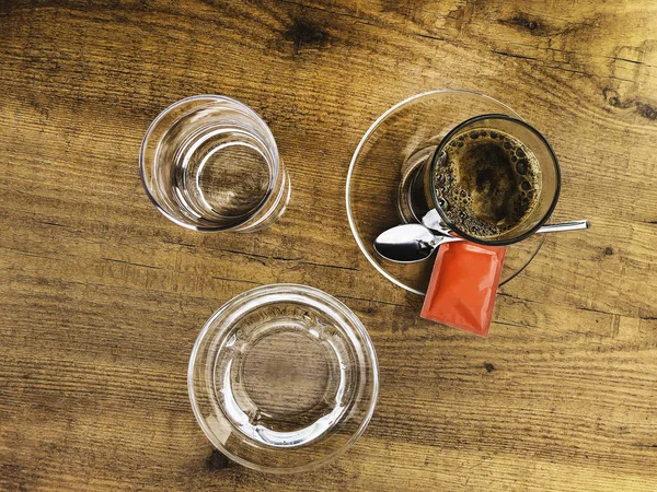 Café fuerte y oscuro en un vaso servido con un vaso de agua sobre una mesa de madera —  Fotos de Stock