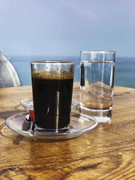 Erős és sötét kávé egy pohár vízzel tálalva egy fa asztalon — Stock Fotó