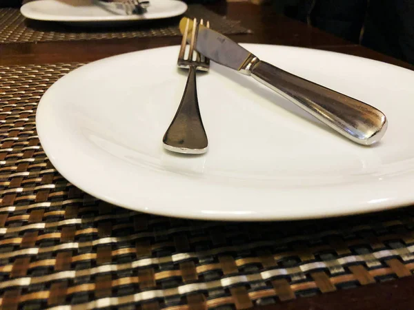 Plato blanco vacío sobre mesa marrón con cuchillo y tenedor — Foto de Stock