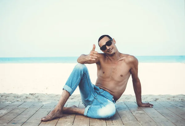 Jonge gespierde man in denim broek rusten en poseren op het strand — Stockfoto