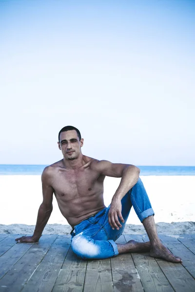 Junger muskulöser Mann in Jeanshose, der am Strand liegt und posiert — Stockfoto