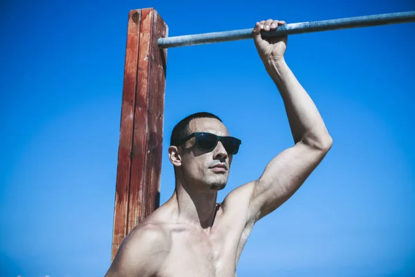 Joven musculoso descansando y posando en la playa. Usar gafas de sol — Foto de Stock