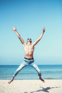 Genç kaslı adam sahilde dinleniyor ve poz veriyor. Havaya zıpla