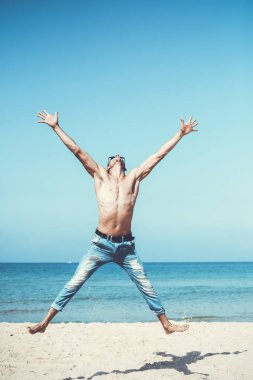 Genç kaslı adam sahilde dinleniyor ve poz veriyor. Havaya zıpla