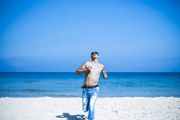 Joven musculoso descansando y posando en la playa. Corre hacia nosotros — Foto de Stock