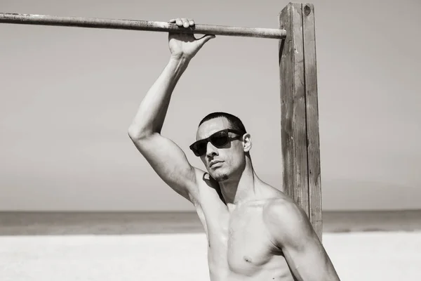 Joven musculoso descansando y posando en la playa. Usar gafas de sol — Foto de Stock