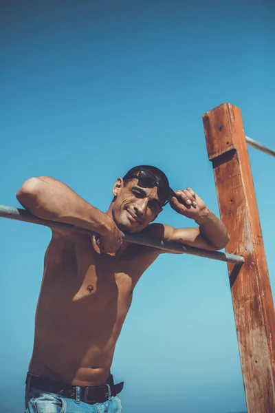 Jonge gespierde man rustend en poserend op het strand. Zonnebrillen dragen — Stockfoto