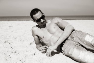 Genç kaslı adam sahilde dinleniyor ve poz veriyor.. 