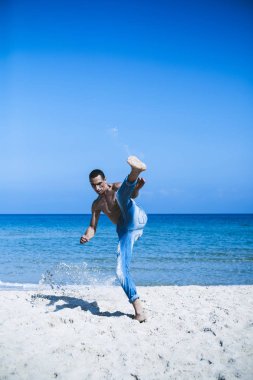 Genç kaslı adam sahilde dinleniyor ve poz veriyor. Sahile taşınıyor.