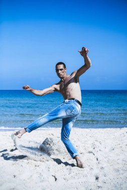 Genç kaslı adam sahilde dinleniyor ve poz veriyor. Sahile taşınıyor.
