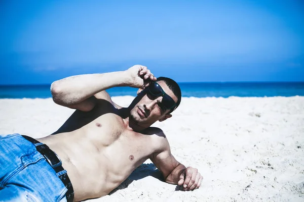 Junger muskulöser Mann ruht sich aus und posiert am Strand. — Stockfoto
