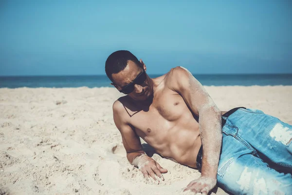 Joven musculoso descansando y posando en la playa . — Foto de Stock