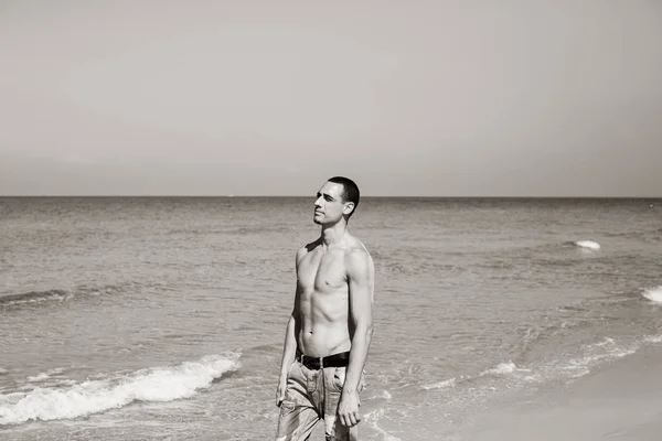 若い筋肉質の男が休んでビーチでポーズをとってる若い男が海を歩いている — ストック写真