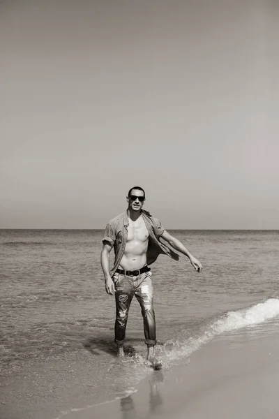 Jeune homme musclé se reposant et posant sur la plage. Un jeune homme marche au bord de la mer — Photo